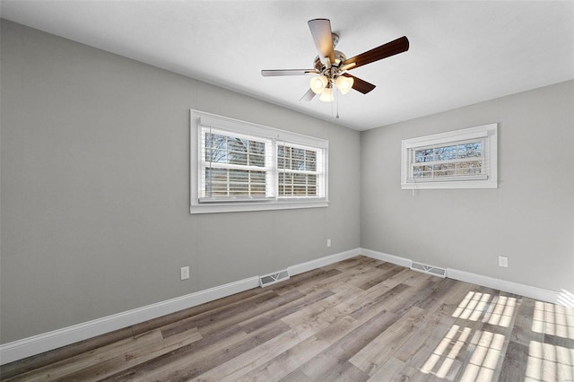 unfurnished room with ceiling fan, wood finished floors, visible vents, and baseboards