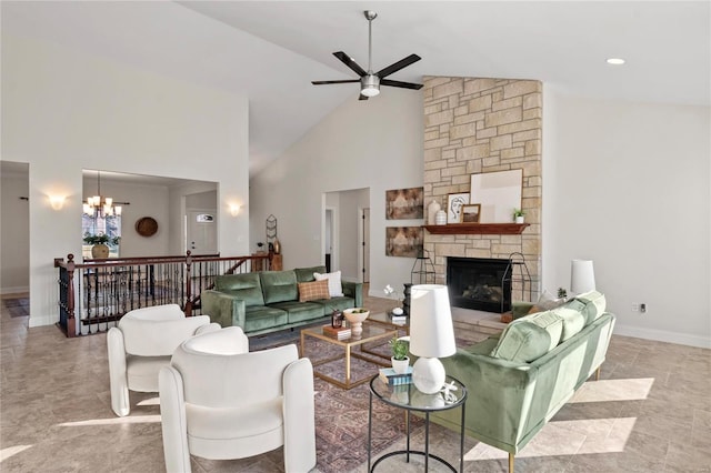 living area with baseboards, high vaulted ceiling, a stone fireplace, and ceiling fan with notable chandelier