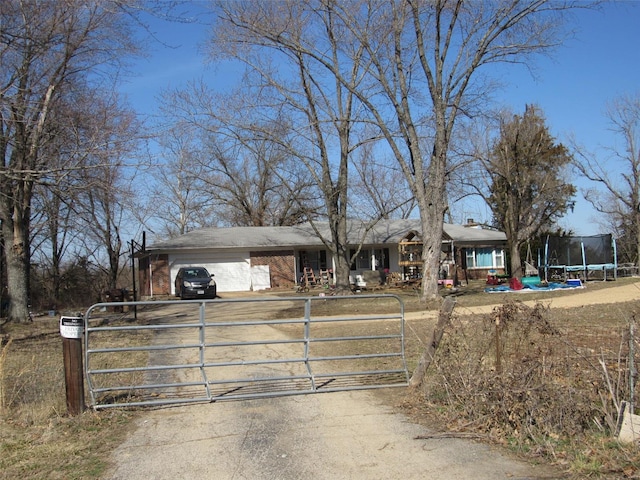 single story home with driveway, brick siding, a trampoline, and a gate