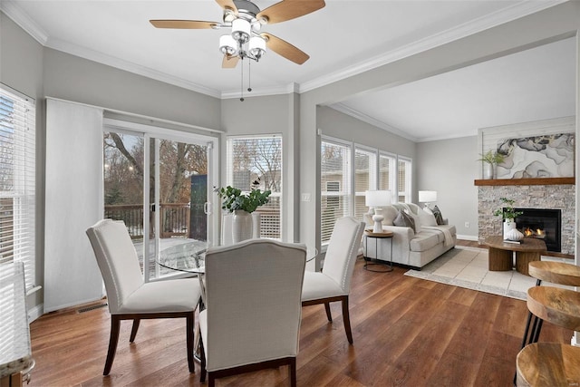 dining space with crown molding, baseboards, wood finished floors, and a stone fireplace