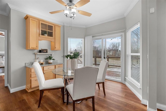 dining area featuring a ceiling fan, crown molding, baseboards, and wood finished floors