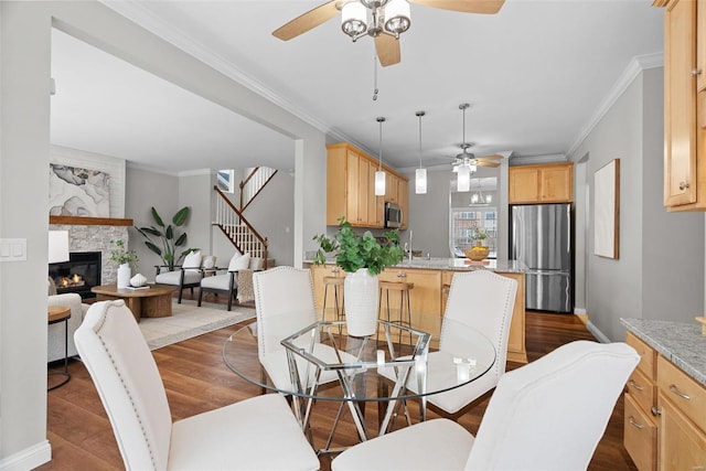 dining room with stairs, a glass covered fireplace, crown molding, and wood finished floors