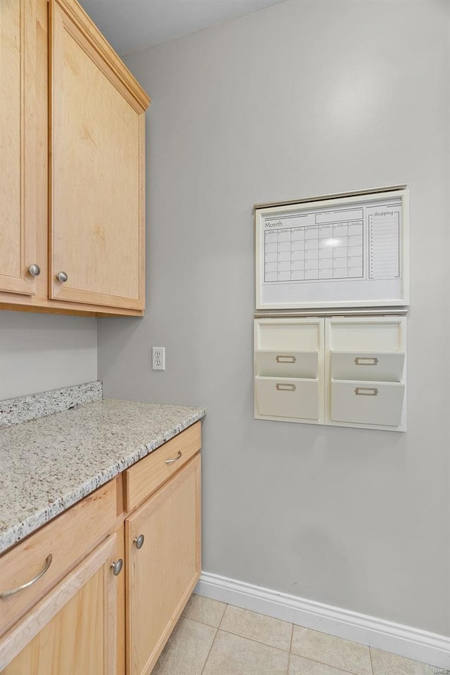 kitchen with light stone countertops, light tile patterned floors, baseboards, and light brown cabinetry