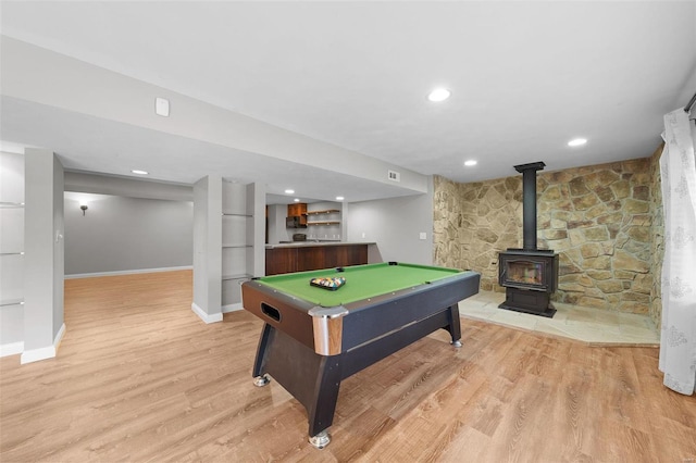 recreation room featuring baseboards, recessed lighting, a wood stove, and light wood-style floors