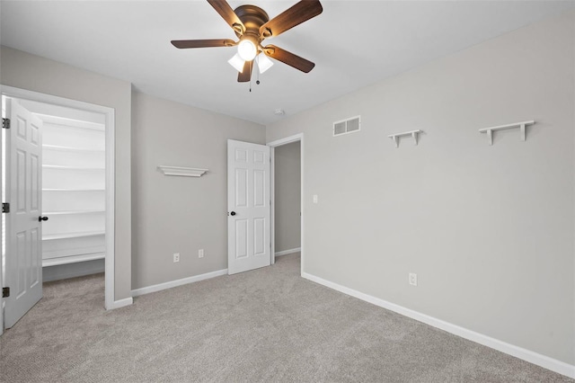 unfurnished bedroom with ceiling fan, carpet flooring, visible vents, baseboards, and a walk in closet