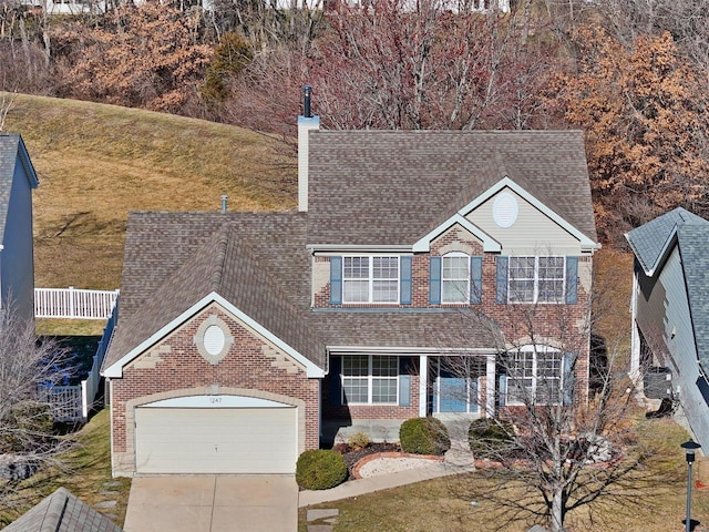 traditional-style home featuring brick siding, a chimney, a shingled roof, concrete driveway, and a garage