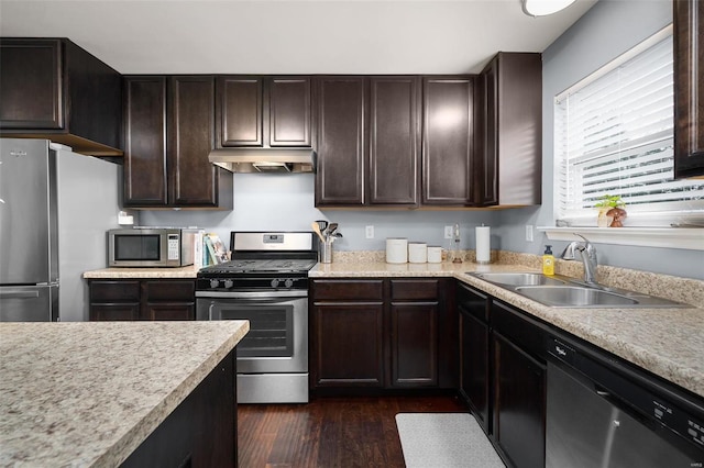 kitchen featuring dark brown cabinetry, appliances with stainless steel finishes, light countertops, under cabinet range hood, and a sink