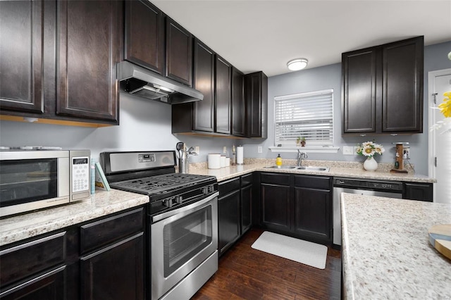 kitchen featuring dark brown cabinetry, under cabinet range hood, a sink, appliances with stainless steel finishes, and dark wood-style floors