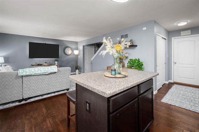 kitchen featuring dark wood-style flooring, visible vents, light countertops, dark brown cabinets, and a center island