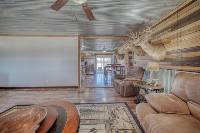 living room featuring baseboards, wooden walls, wood finished floors, and a ceiling fan