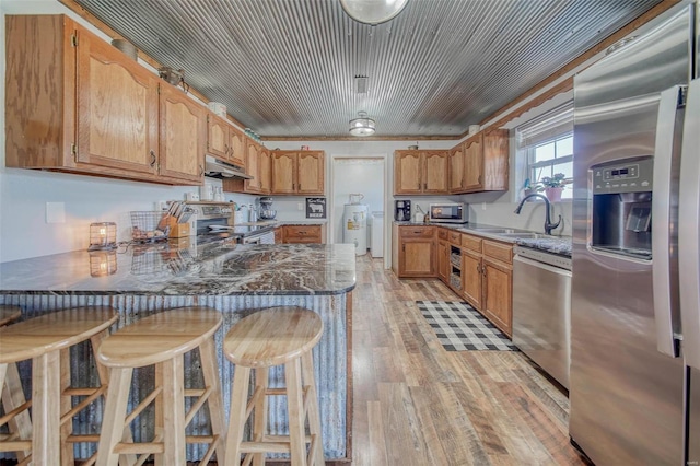 kitchen with a peninsula, light wood-style floors, under cabinet range hood, appliances with stainless steel finishes, and electric water heater