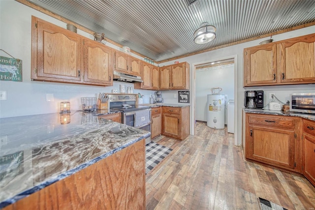 kitchen with under cabinet range hood, light wood-type flooring, water heater, dark stone countertops, and appliances with stainless steel finishes