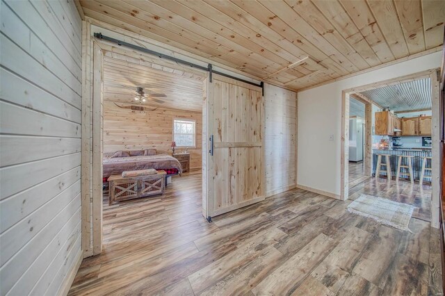 interior space featuring wooden walls, a ceiling fan, light wood finished floors, a barn door, and wooden ceiling