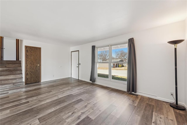 unfurnished living room with stairs, baseboards, and wood finished floors