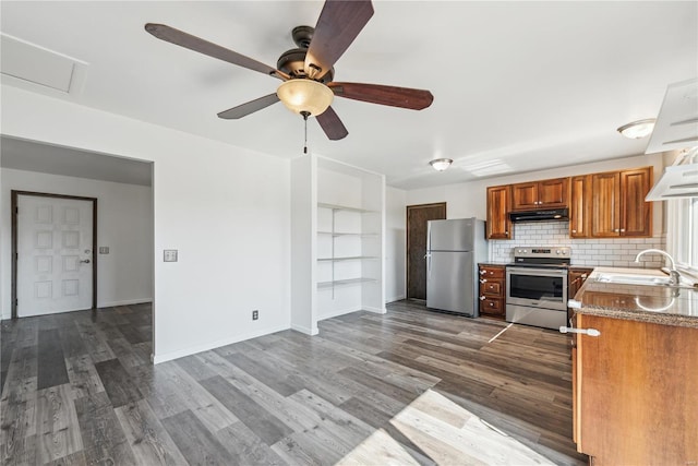 kitchen with under cabinet range hood, stainless steel appliances, a sink, decorative backsplash, and dark wood-style floors