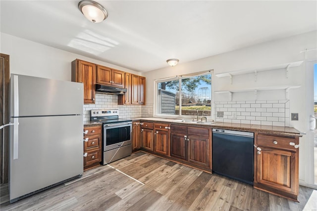 kitchen featuring light wood-style flooring, under cabinet range hood, a sink, appliances with stainless steel finishes, and decorative backsplash