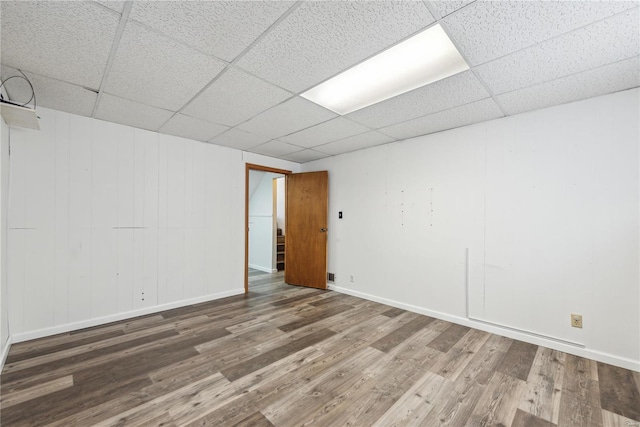 empty room featuring a drop ceiling, wood finished floors, and baseboards