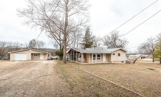 view of front of home with an outbuilding, a detached garage, a chimney, dirt driveway, and covered porch