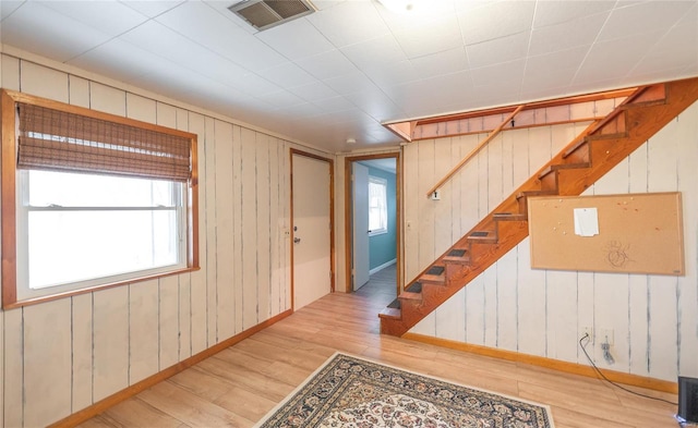 foyer with light wood finished floors, visible vents, wooden walls, baseboards, and stairs