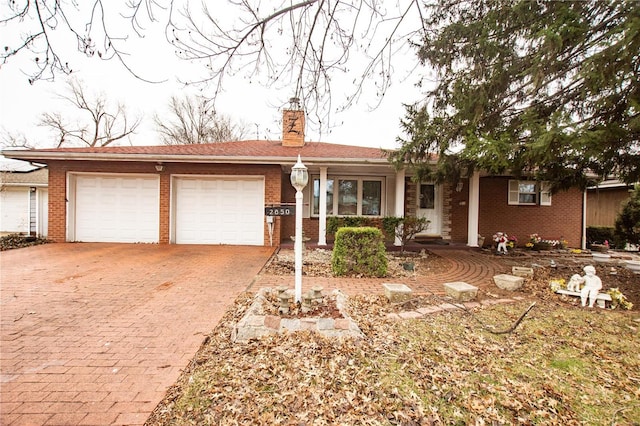 ranch-style house with brick siding, an attached garage, a chimney, and decorative driveway