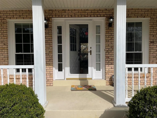 entrance to property with a porch and brick siding