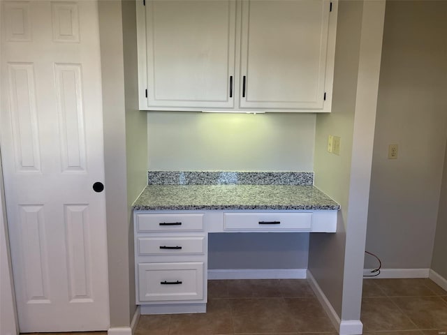 interior space featuring light stone counters, dark tile patterned floors, built in study area, and white cabinetry