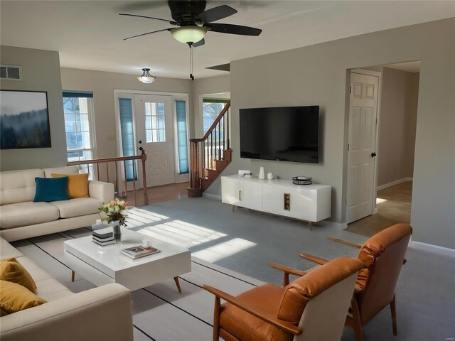 living area with carpet floors, visible vents, stairway, ceiling fan, and baseboards