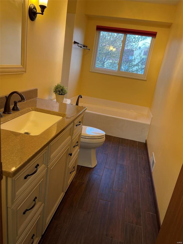 bathroom with baseboards, toilet, wood finished floors, vanity, and a bath