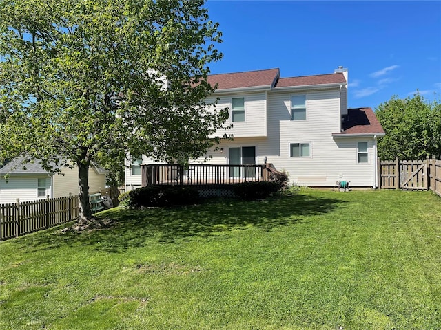 rear view of house featuring a fenced backyard, a chimney, a wooden deck, and a lawn