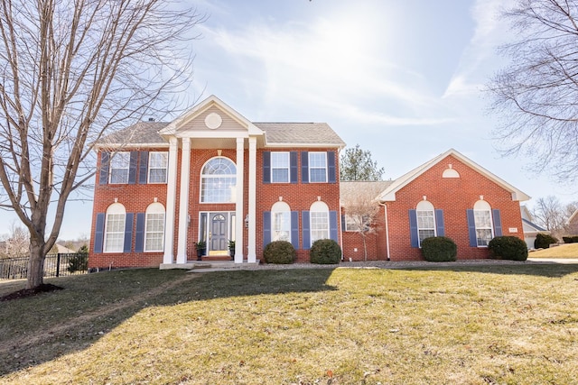 neoclassical home featuring brick siding, fence, and a front yard