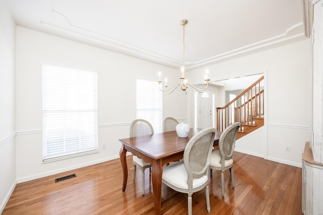 dining room featuring baseboards, visible vents, stairway, wood finished floors, and an inviting chandelier