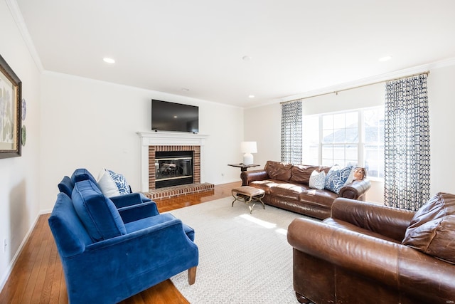 living area with recessed lighting, baseboards, ornamental molding, a brick fireplace, and hardwood / wood-style floors