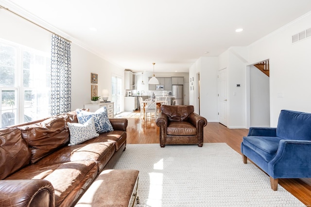 living area with baseboards, light wood-style flooring, visible vents, and crown molding