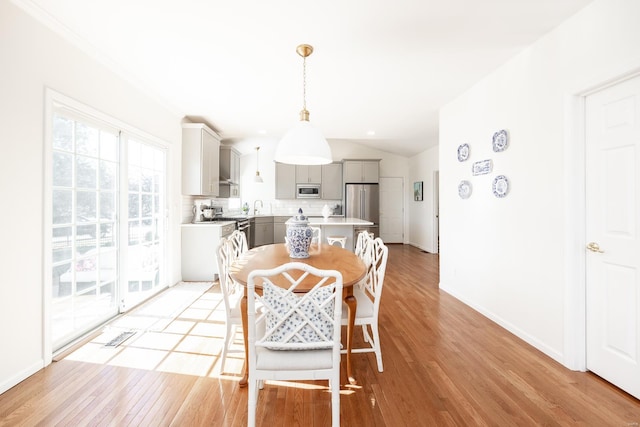 dining space featuring vaulted ceiling, light wood-style flooring, and baseboards