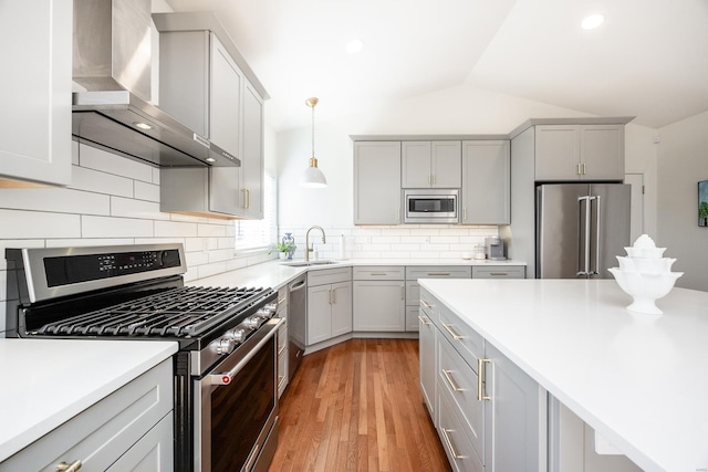 kitchen with lofted ceiling, appliances with stainless steel finishes, gray cabinetry, wall chimney range hood, and a sink