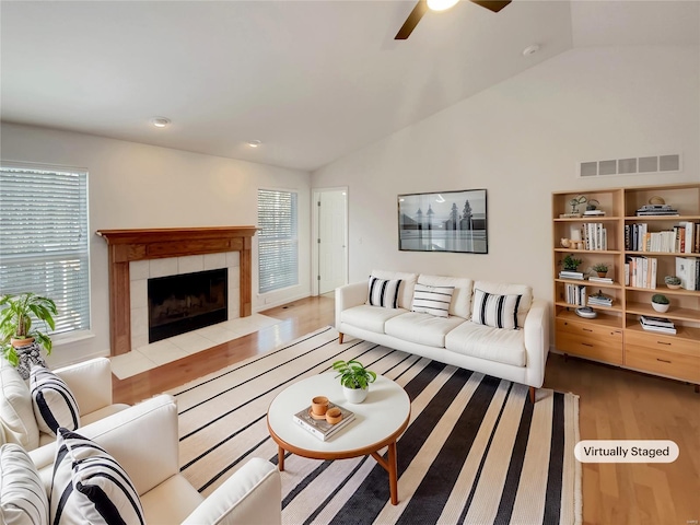 living room featuring lofted ceiling, a tiled fireplace, visible vents, and wood finished floors