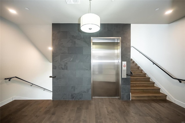 staircase featuring elevator and wood finished floors