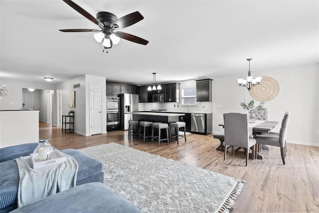 living area with visible vents, baseboards, light wood-style floors, and ceiling fan with notable chandelier