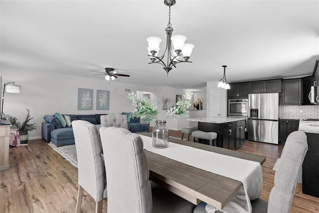 dining space with baseboards, wood finished floors, and ceiling fan with notable chandelier