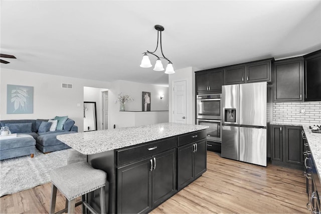 kitchen with dark cabinetry, light wood finished floors, a kitchen island, appliances with stainless steel finishes, and open floor plan