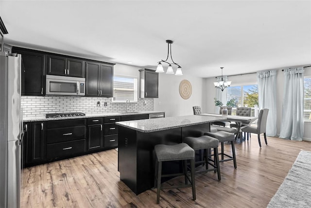 kitchen with a sink, appliances with stainless steel finishes, dark cabinetry, and light wood finished floors