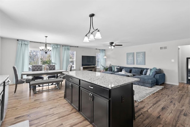 kitchen with visible vents, decorative light fixtures, light wood-style flooring, ceiling fan with notable chandelier, and dark cabinetry