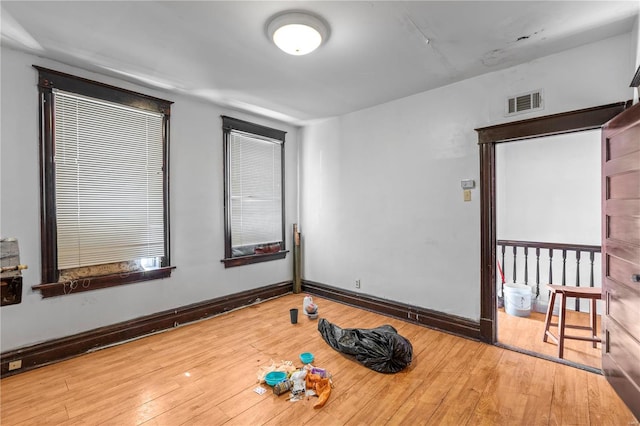 spare room with wood-type flooring, visible vents, and baseboards