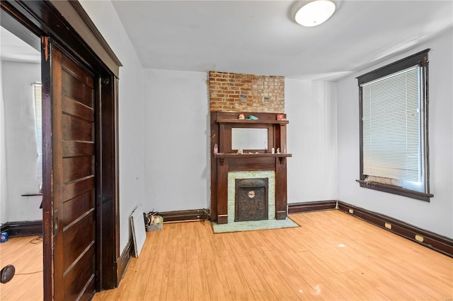 unfurnished living room featuring a brick fireplace, a healthy amount of sunlight, baseboards, and wood finished floors