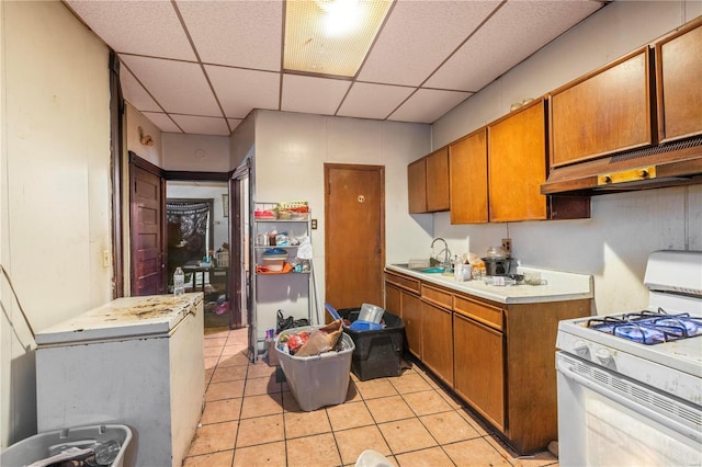 kitchen featuring brown cabinets, white gas stove, a paneled ceiling, light countertops, and under cabinet range hood