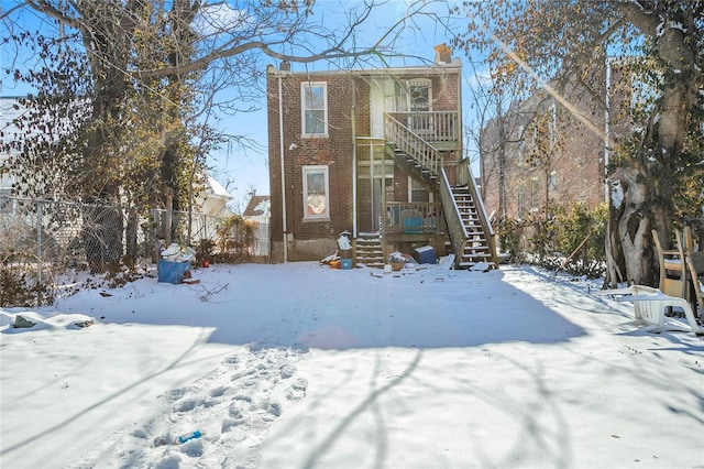 view of front of home featuring a chimney, brick siding, fence, and stairway