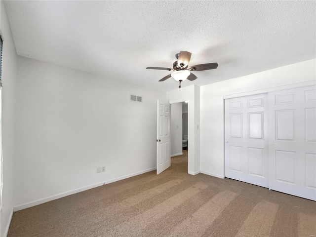 unfurnished bedroom with baseboards, visible vents, a textured ceiling, carpet floors, and a closet