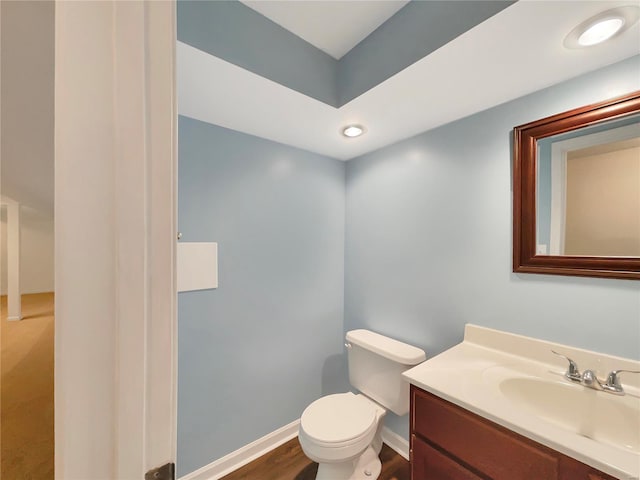 half bath with wood finished floors, vanity, toilet, and baseboards