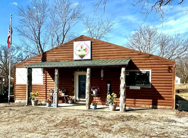 view of front facade featuring covered porch, faux log siding, and metal roof