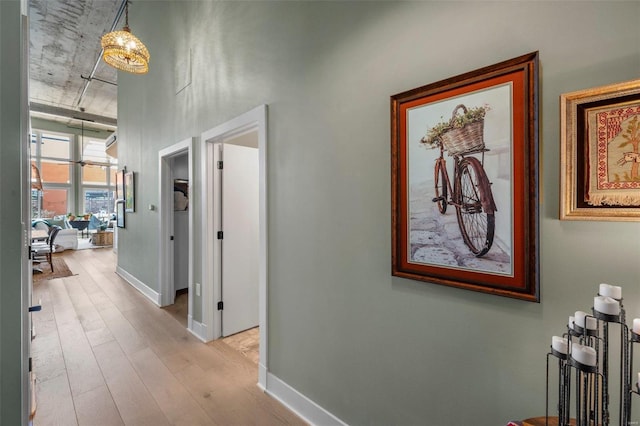 hall with baseboards, a chandelier, and wood finished floors